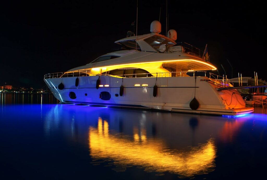 Large yacht with bright, LED lighting reflecting off the water.